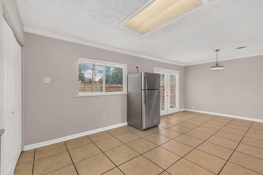 Bright kitchen with a wide window, tile flooring and a stainless steel refrigerator, offering a fresh and inviting space.