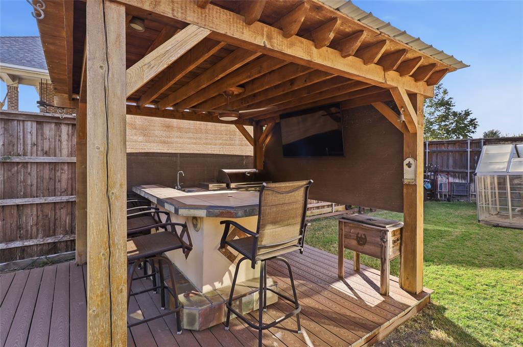 Outdoor Kitchen features custom cedar arbor, gas grill, sink, TV, bar seating, and refrigerator.