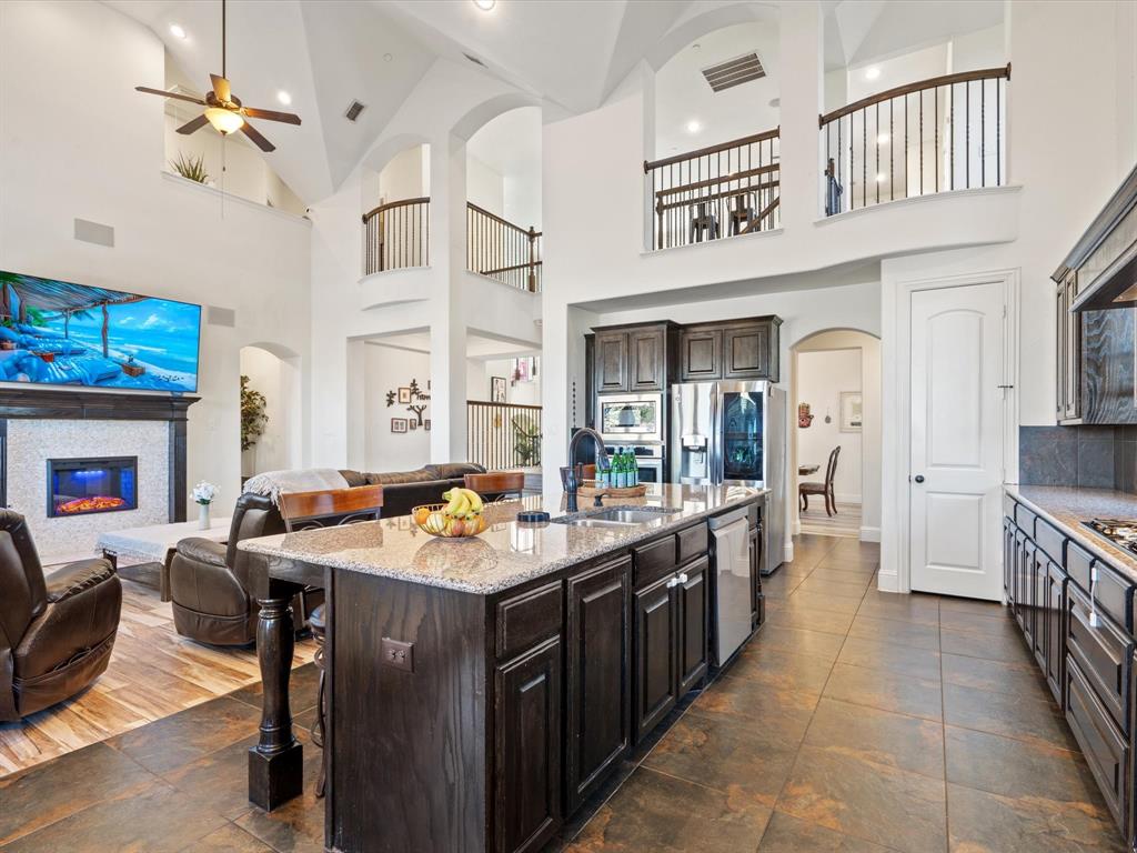 Kitchen with arched walkways, dark brown cabinets, open floor plan, light stone countertops, and high vaulted ceiling