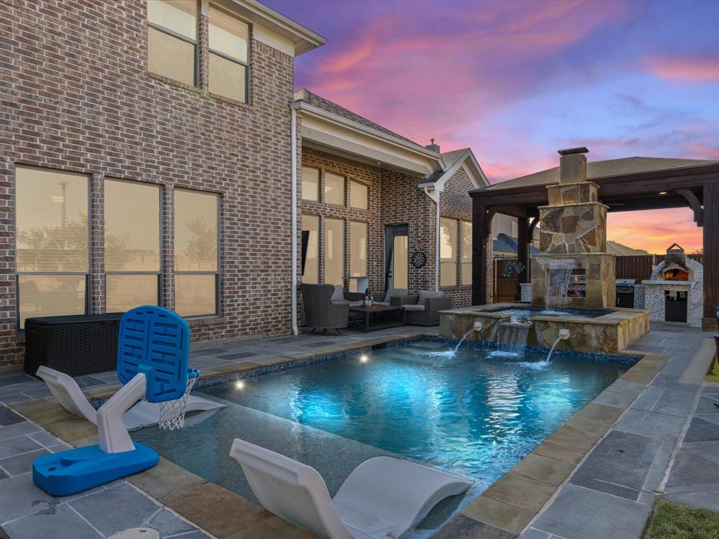 View of swimming pool featuring an outdoor stone fireplace, an outdoor kitchen, a patio area, and a pool with connected hot tub