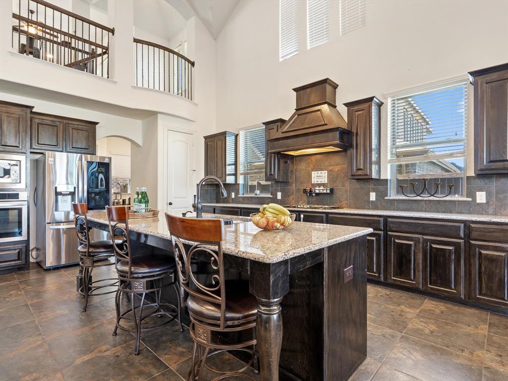 Kitchen featuring dark brown cabinetry, appliances with stainless steel finishes, light stone counters, a kitchen bar, and a kitchen island with sink
