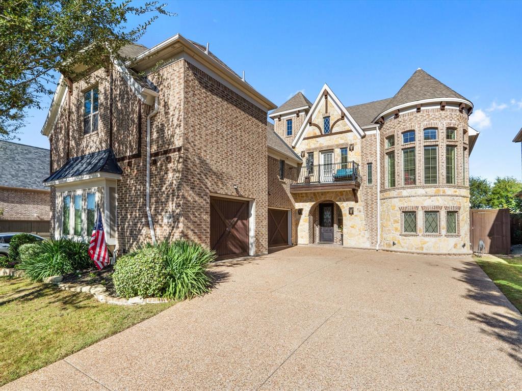 This stunning French country-inspired facade boasts a charming balcony, warm brick siding, and an expansive three-car garage, complete with a beautiful, lengthy driveway perfect for accommodating additional guest parking.
