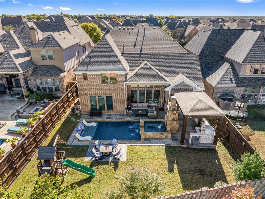 Backyard aerial view of a premium Allen home with a spacious, fully fenced backyard featuring a resort-style pool, attached spa, multiple covered patios, outdoor seating with fire features, playset, mature landscaping, and ample entertaining space. Backyard aerial view of a premium Allen home with a spacious, fully fenced backyard featuring a resort-style pool, attached spa, multiple covered patios, outdoor seating with fire features, playset, mature landscaping, and ample entertaining space.