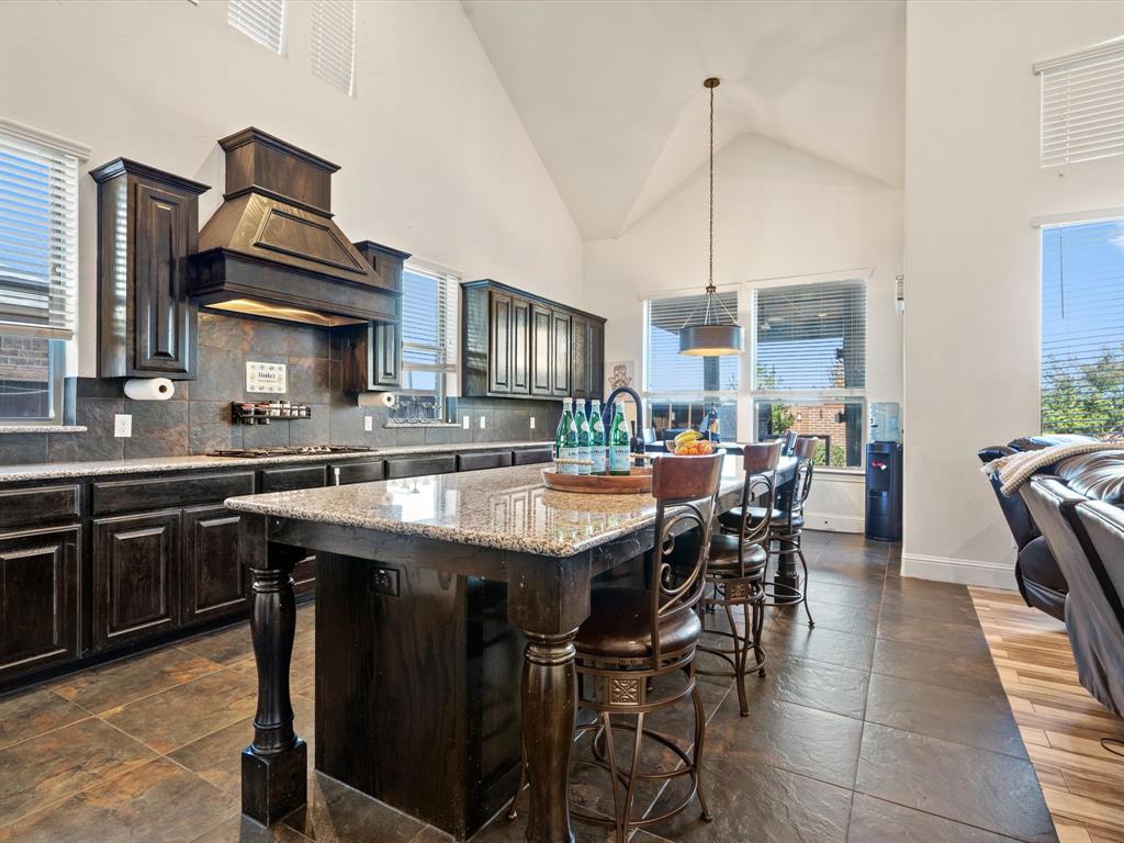 Kitchen featuring a kitchen breakfast bar, high vaulted ceiling, a kitchen island with sink, dark brown cabinetry, and light stone countertops