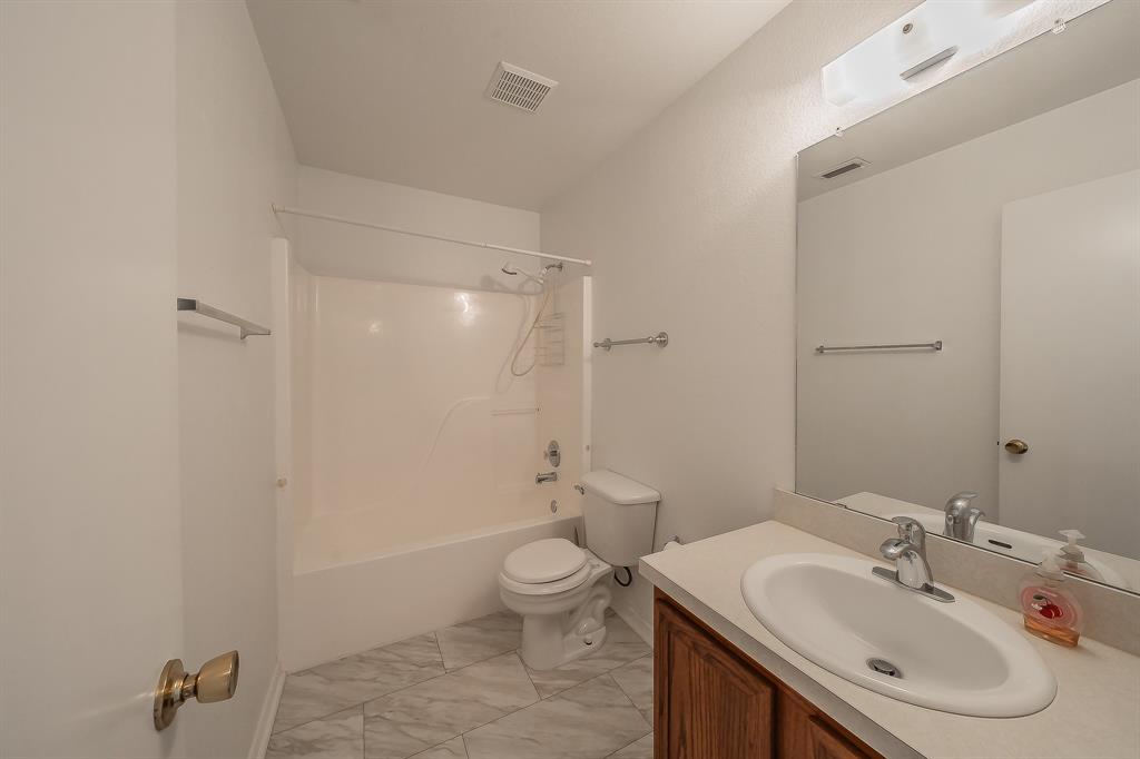 Bathroom featuring a vanity with an integrated basin, wood-finish cabinetry, a large wall-mounted mirror, and tile flooring arranged in a diagonal pattern