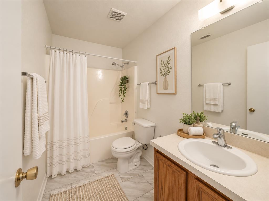 Full bathroom featuring wood-finish vanity cabinetry, integrated sink basin, solid-surface countertop, full-width vanity mirror, and a tub-shower combination with a surround