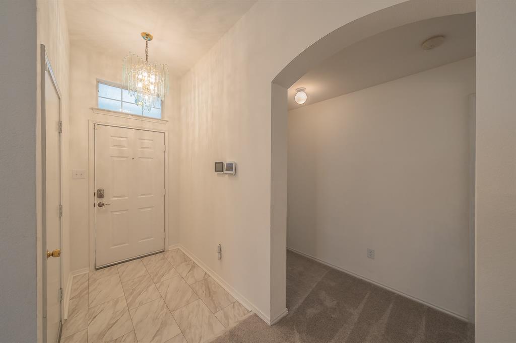 Entryway featuring high ceilings, a crystal-style chandelier, a transom window above the door, stone-finish tile flooring, and an arched doorway