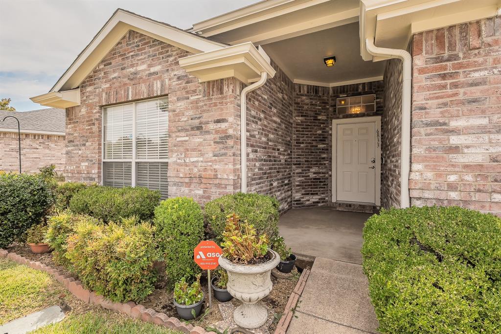 Multi-toned brick exterior featuring a covered entryway, concrete front porch, transom window above the entry door, and manicured shrubbery