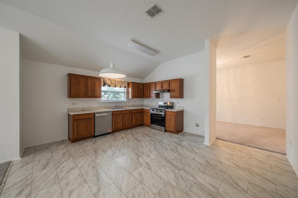 Kitchen featuring wood cabinetry, stone-finish tile flooring, a stainless steel dishwasher, a slide-in range, and a vaulted ceiling with a pendant light fixture