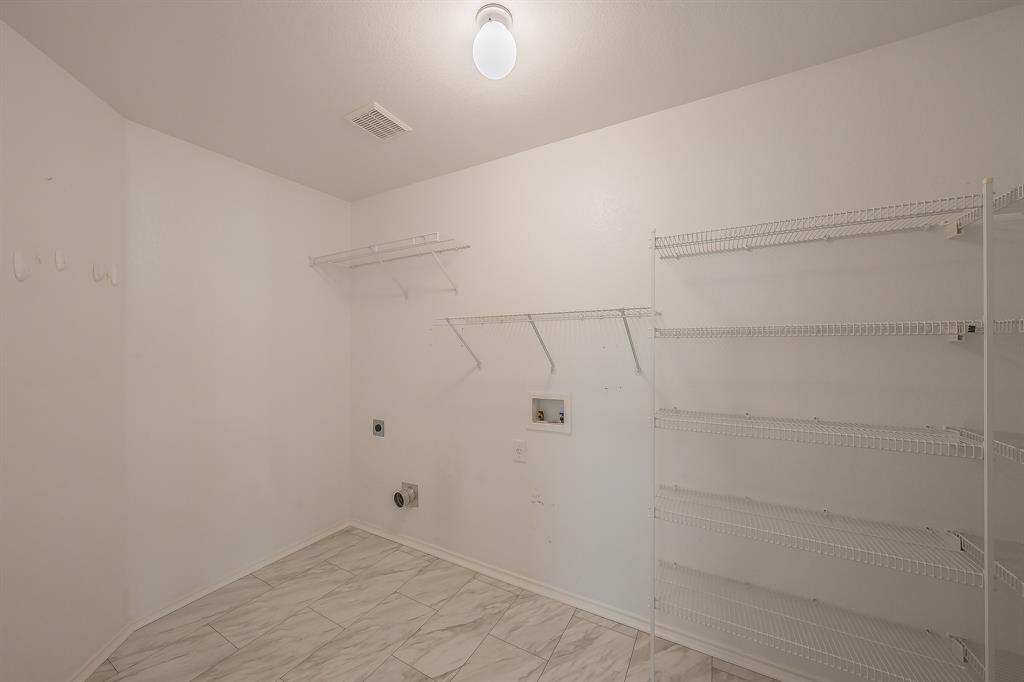 Utility area featuring stone-patterned tile flooring, multi-tier wire shelving, and dedicated utility hookups