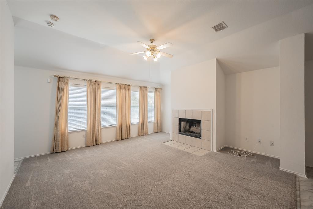 Living area featuring vaulted ceilings, a fireplace with neutral tile surround and hearth, carpeted flooring, and multiple windows