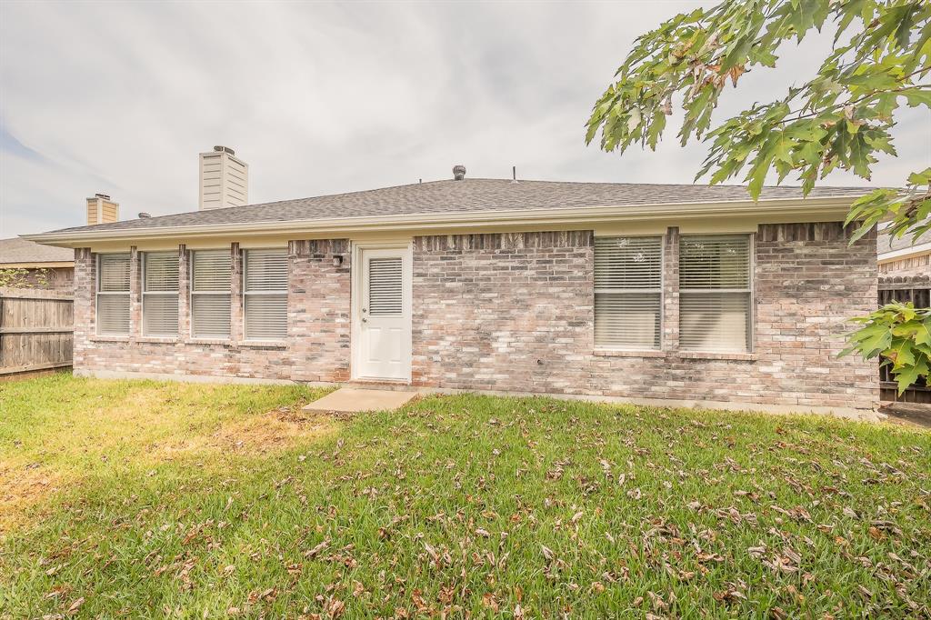 Multi-tone brick exterior featuring a single-story profile, rear access door, shingle roof, two masonry chimneys, and multiple windows with horizontal blinds