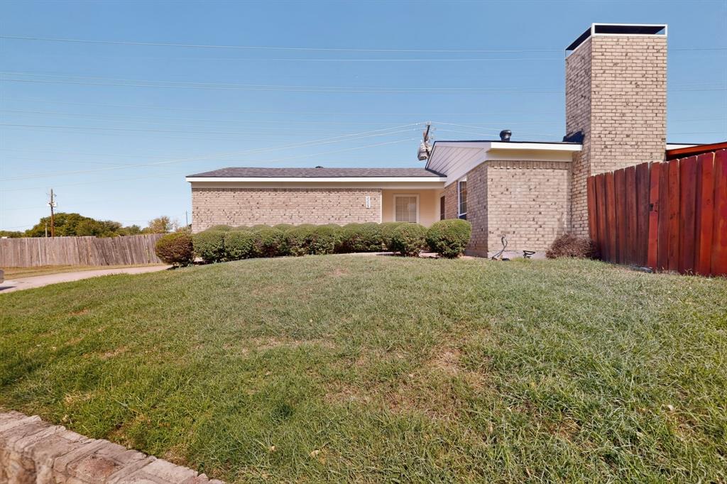 Single-story brick exterior featuring a prominent masonry chimney, stone landscape edging, and mature shrubs
