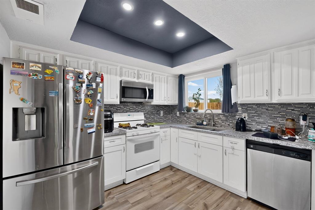 Kitchen featuring white cabinetry, stone-finish countertops, mosaic tile backsplash, recessed tray ceiling, and wood-finish flooring