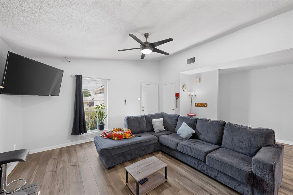 Living area featuring wood-finish flooring, vaulted ceilings, and a ceiling fan with integrated lighting