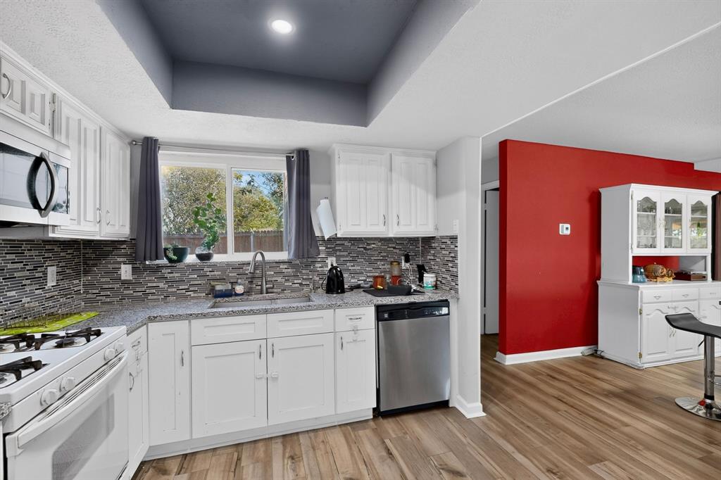 Kitchen featuring white cabinetry, stone-finish countertops, multi-toned tile backsplash, stainless steel dishwasher, and wood-finish flooring