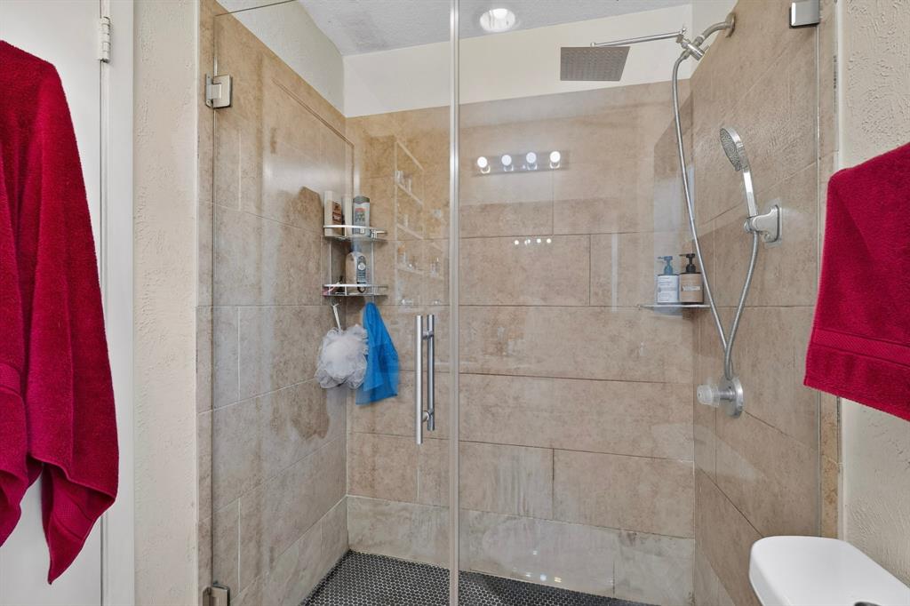 Walk-in shower featuring floor-to-ceiling neutral tile, glass enclosure, ceiling-mounted rainfall showerhead, and handheld sprayer