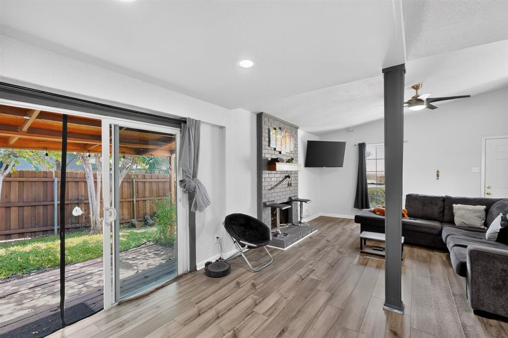 Living area featuring wood-finish flooring, a gray brick fireplace with a wood mantel, a ceiling fan, and sliding glass doors opening to a covered patio