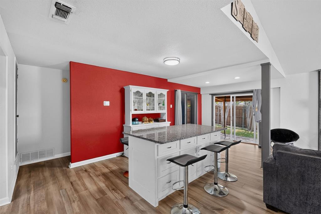 Kitchen featuring a central island with a stone-finish countertop, white built-in cabinetry, wood-finish flooring, and sliding glass doors