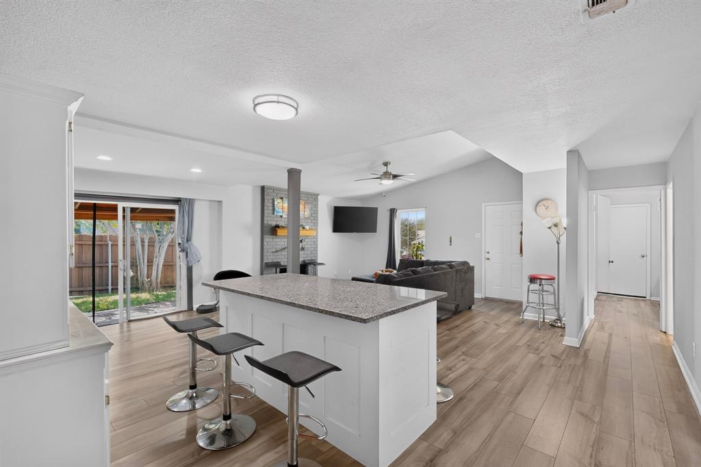 Open concept interior featuring wood-finish flooring, a central kitchen island with a stone-finish countertop, vaulted ceilings, and a fireplace with brick masonry