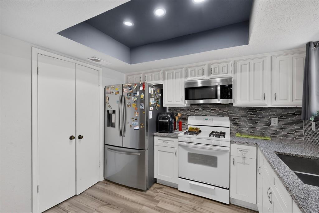 Kitchen featuring white shaker-style cabinetry, stone-finish countertops, decorative mosaic tile backsplash, recessed ceiling lighting, and wood-finish flooring
