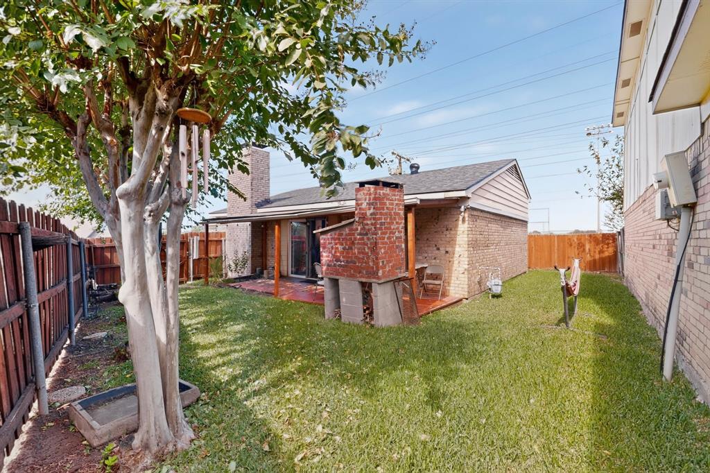 Rear exterior featuring a brick fireplace, covered patio, wood fencing, and mature landscaping