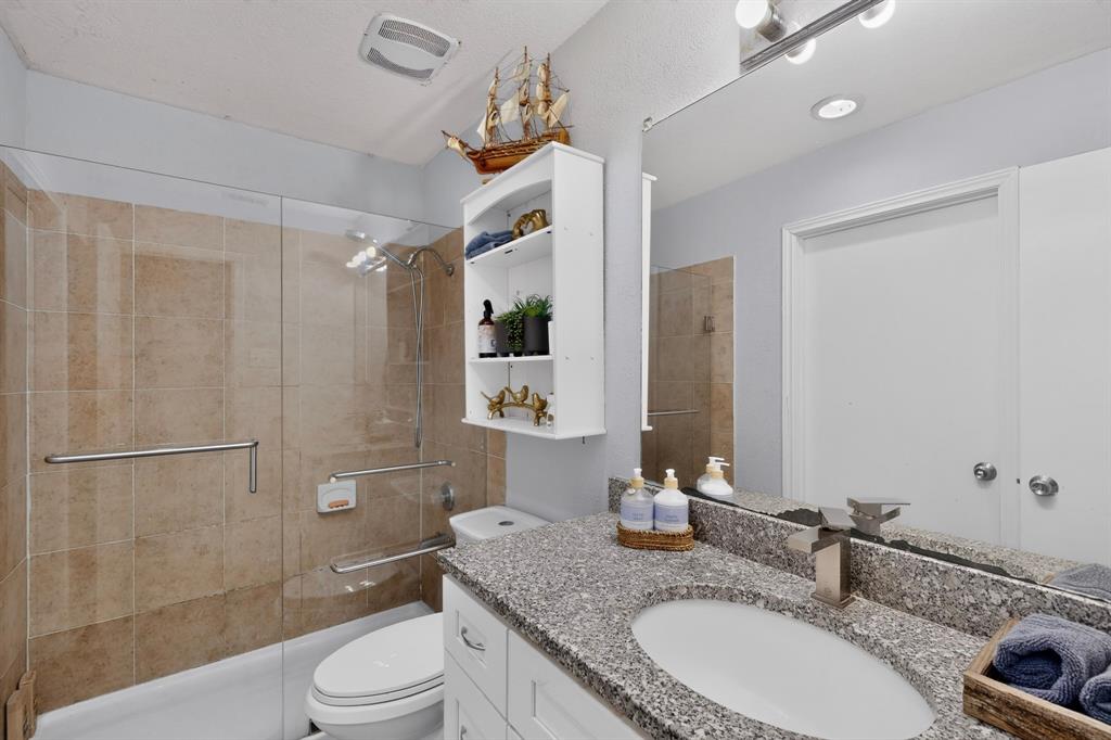 Bathroom featuring a vanity with a stone-composite countertop, integrated oval basin, and metallic fixtures, complemented by a tiled shower enclosure with a glass panel and mounted support rails