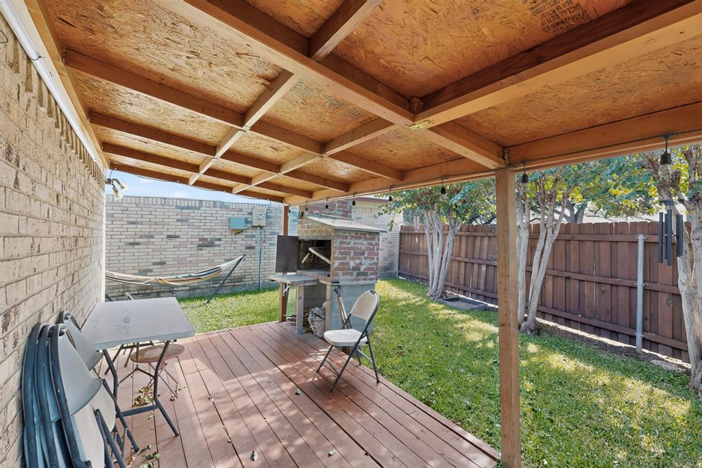 Covered outdoor deck with wood-finish flooring, exposed timber ceiling beams, and a built-in masonry grill