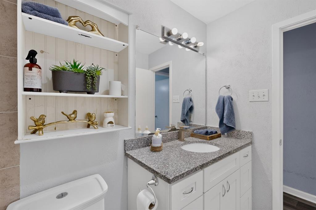 Built-in recessed shelving with beadboard backing, white vanity cabinet with stone-finish countertop, undermount sink, and four-light wall-mounted vanity fixture