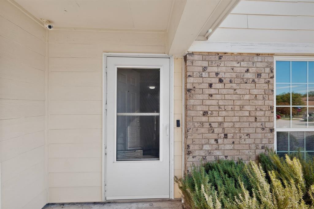 Entryway featuring a white storm door, beige horizontal lap siding, tan brick masonry, and a multi-pane window Entryway featuring a white storm door, beige horizontal lap siding, tan brick masonry, and a multi-pane window