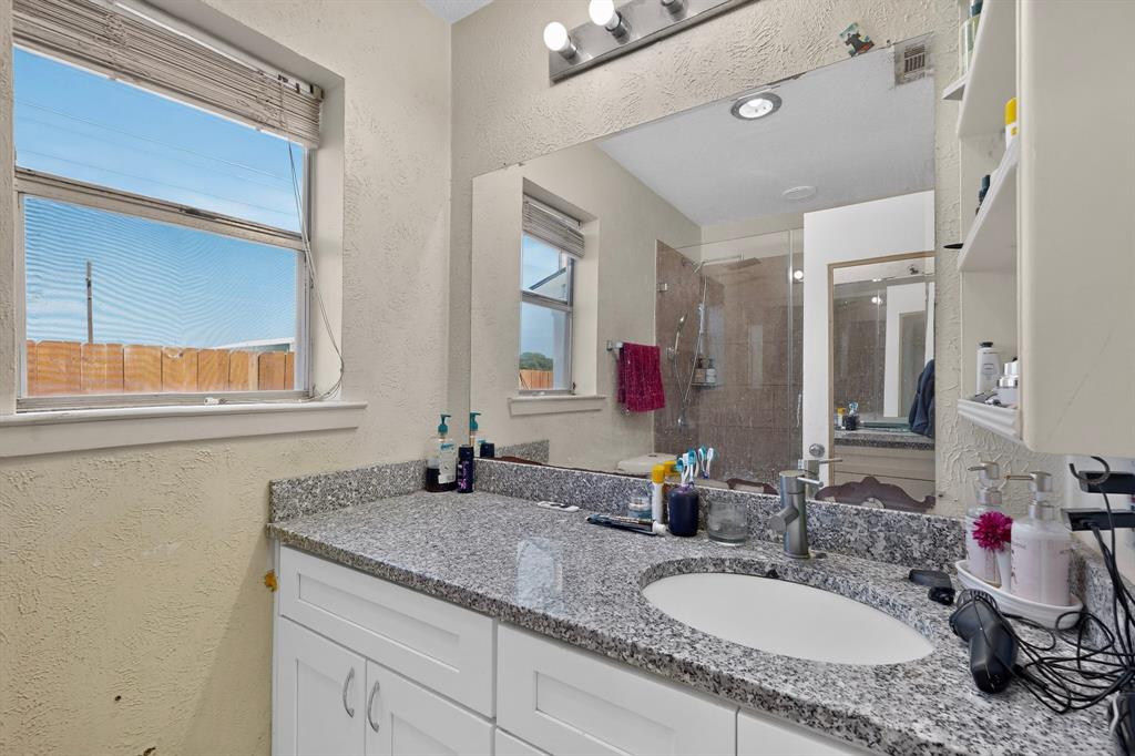 Bathroom featuring white cabinetry, stone-surface countertop with an integrated undermount sink, large wall-mounted mirror, and glass-enclosed shower