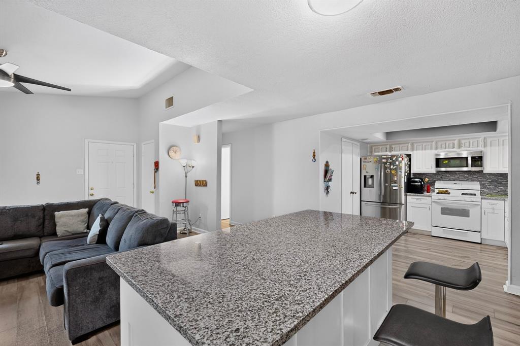 Kitchen featuring a stone-topped island, white cabinetry, integrated stainless steel appliances, and wood-finish flooring