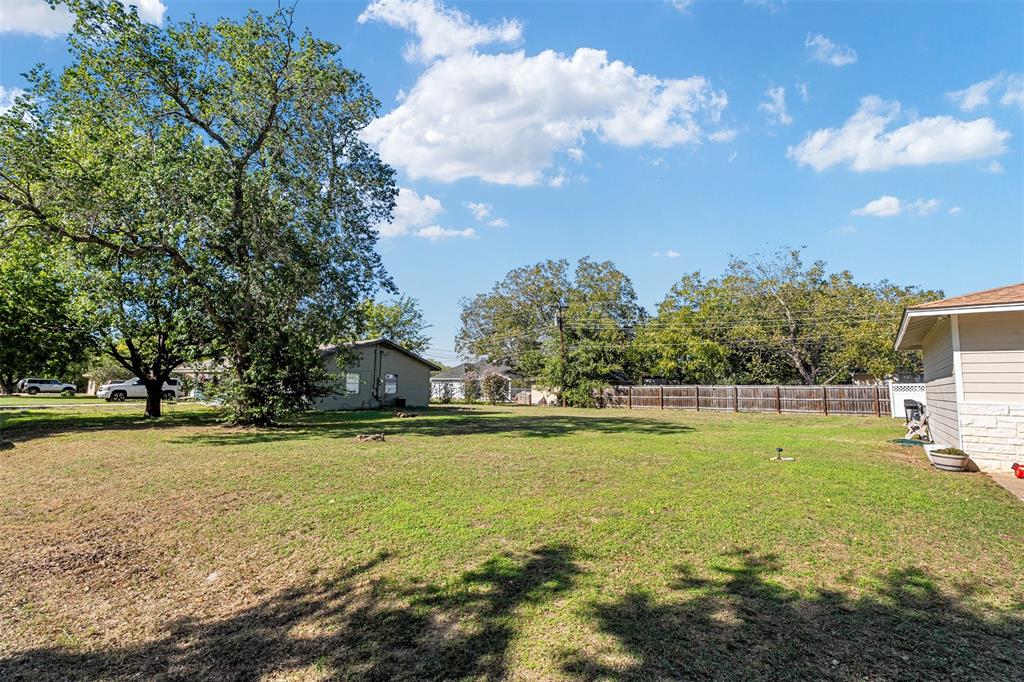 Expansive backyard featuring a large grass lawn, mature trees, and wooden perimeter fencing