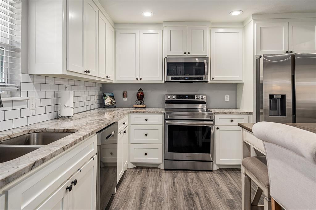 Kitchen featuring white shaker cabinetry, stone-surface countertops, subway tile backsplash, stainless steel appliances, and wood-finish flooring