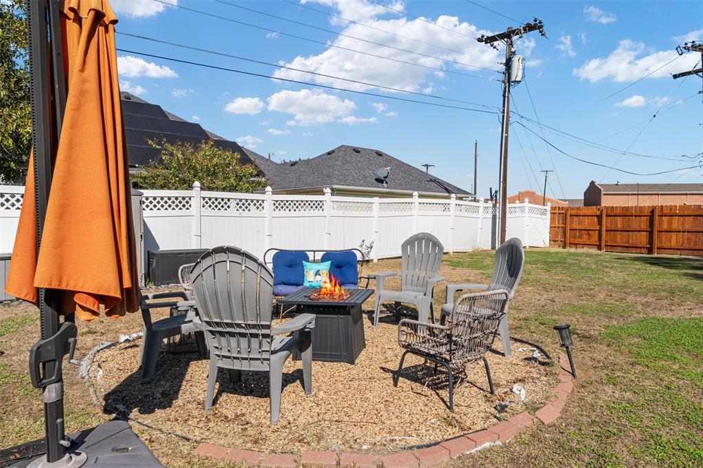 Backyard featuring a circular gravel patio area with a brick-paver border and a white vinyl perimeter fence