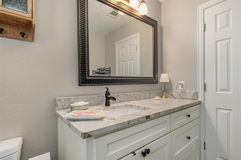 Vanity featuring a stone countertop with an integrated basin, matte black faucet, white shaker-style cabinetry, and a framed mirror