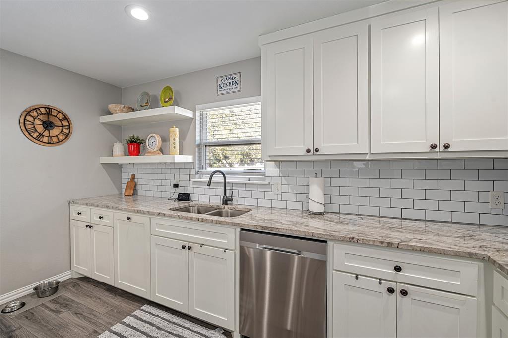 Kitchen featuring white shaker-style cabinetry, stone-patterned countertops, subway tile backsplash, floating shelving, and stainless steel dishwasher