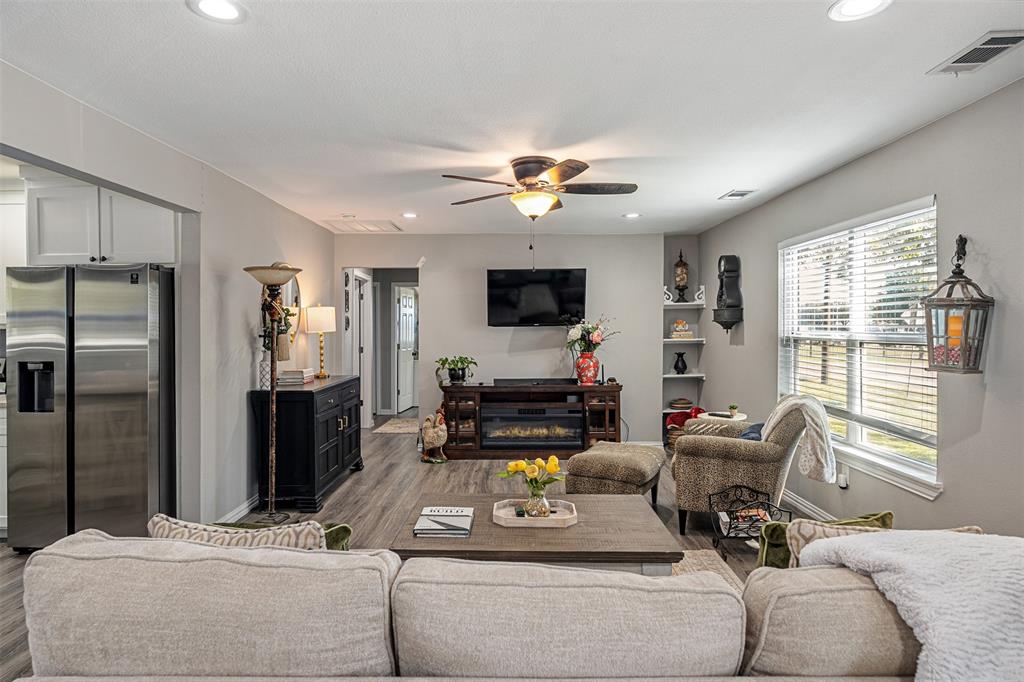 Open-concept interior featuring wood-finish flooring, recessed lighting, a ceiling fan, built-in shelving, and a large window Open-concept interior featuring wood-finish flooring, recessed lighting, a ceiling fan, built-in shelving, and a large window