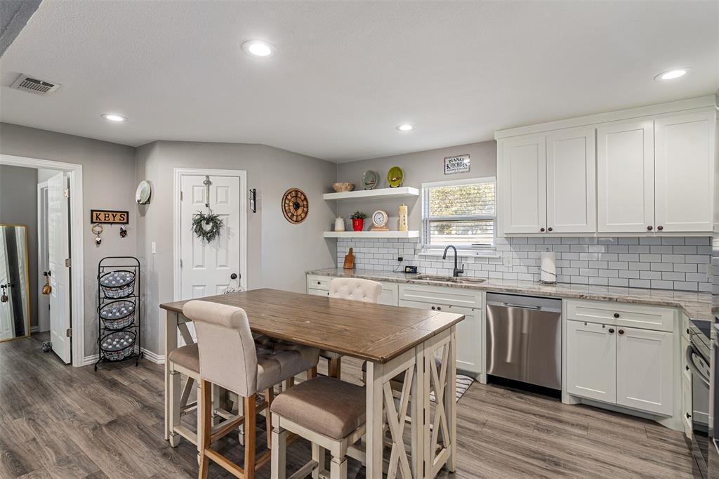 Kitchen featuring white shaker-style cabinetry, stone countertops, subway tile backsplash, recessed lighting, and wood-finish flooring Kitchen featuring white shaker-style cabinetry, stone countertops, subway tile backsplash, recessed lighting, and wood-finish flooring