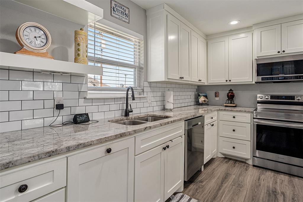 Kitchen featuring white shaker-style cabinetry, stone countertops, a subway tile backsplash, stainless steel appliances, and wood-finish flooring