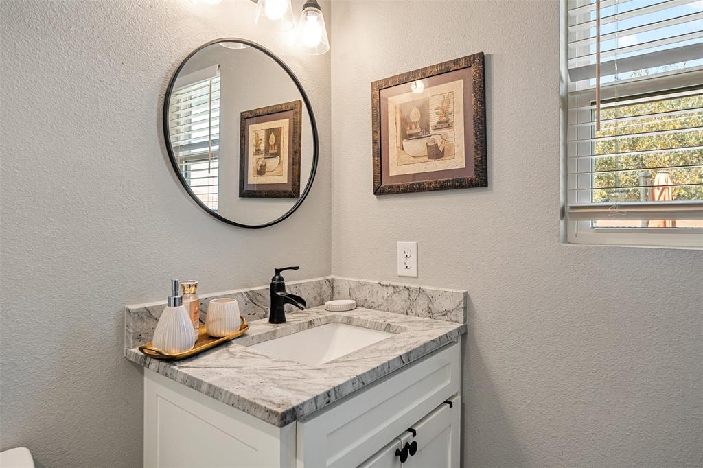 Vanity featuring a white cabinet, patterned stone countertop with an integrated rectangular sink, matte black faucet, and a circular wall-mounted mirror
