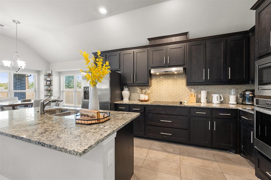 Kitchen featuring dark-finish cabinetry, stone-surface countertops, neutral tile backsplash, stainless steel built-in appliances, and vaulted ceilings