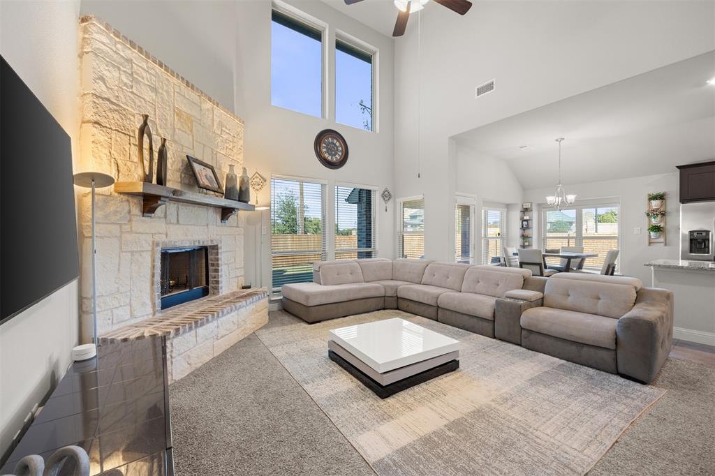 Double-height ceiling, floor-to-ceiling stone fireplace with a natural wood mantel, and expansive windows