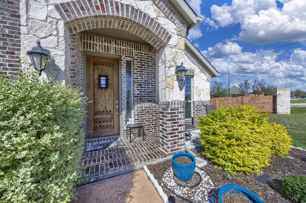 Exterior entry featuring a multi-textured stone and brick façade, arched brick detailing, a stained wood entry door with iron hardware, and wall-mounted exterior lanterns