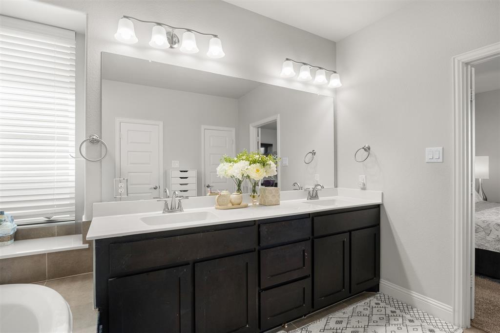 Double vanity featuring dark cabinetry, dual undermount sinks, solid surface countertops, two four-light fixtures, and a full-width wall mirror