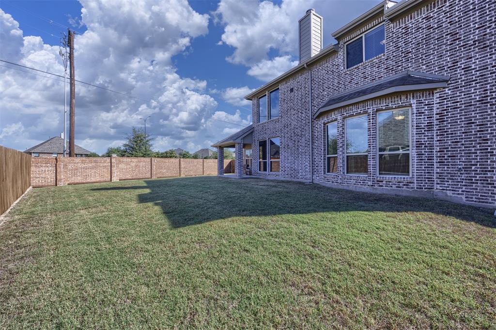 Backyard featuring a manicured lawn, brick exterior siding, chimney, covered patio, and perimeter brick wall