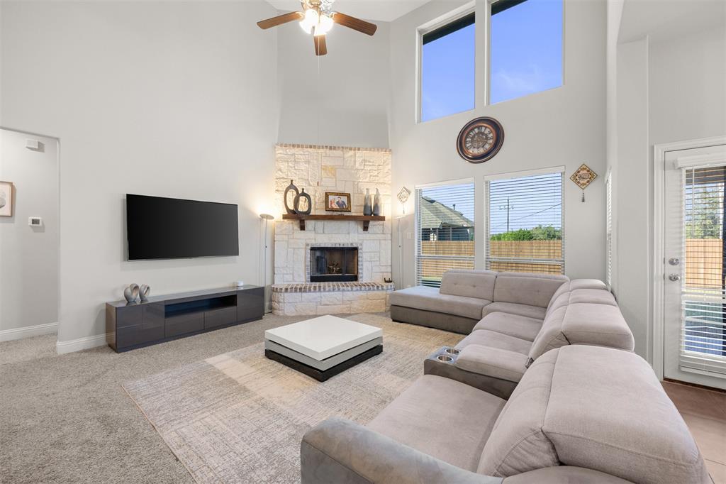 Living room featuring vaulted ceilings, floor-to-ceiling stone fireplace with a wood mantel, oversized windows, and a ceiling fan