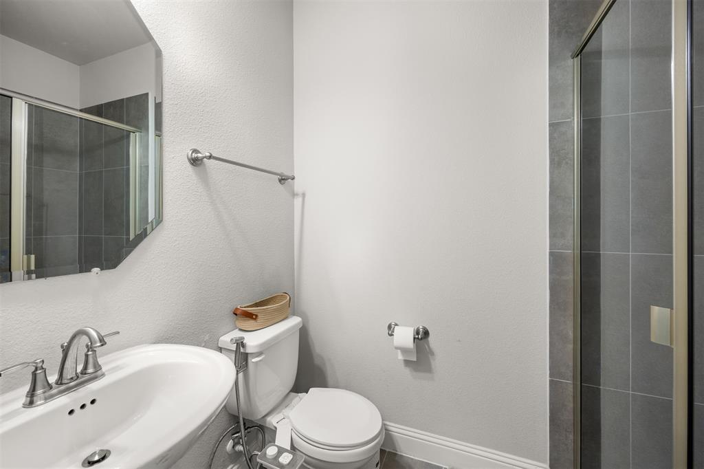 Bathroom featuring a white pedestal sink with a metallic faucet, a geometric wall mirror, and a glass-enclosed shower with large-format grey tile surround