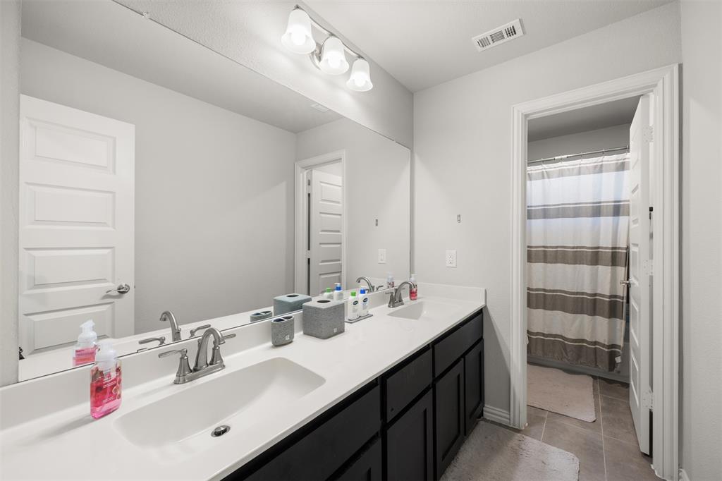 Double vanity with white solid-surface countertops, dark cabinetry, full-width wall mirror, and three-bulb vanity light fixture