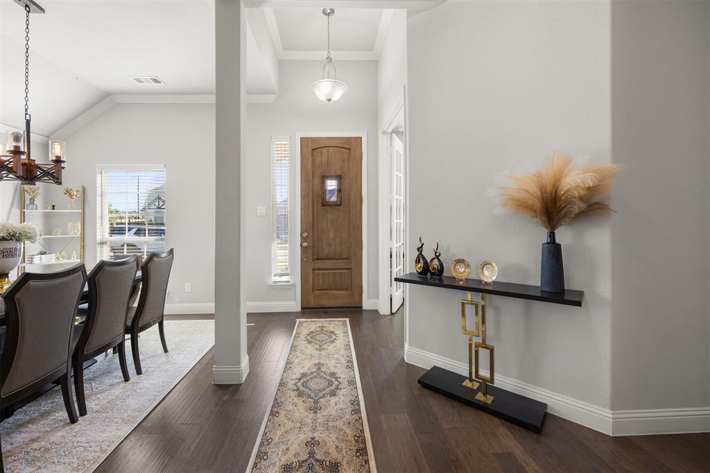 Foyer entry featuring dark wood-finish flooring, a solid wood front door with a decorative inset window, high ceilings with crown molding, and two pendant light fixtures